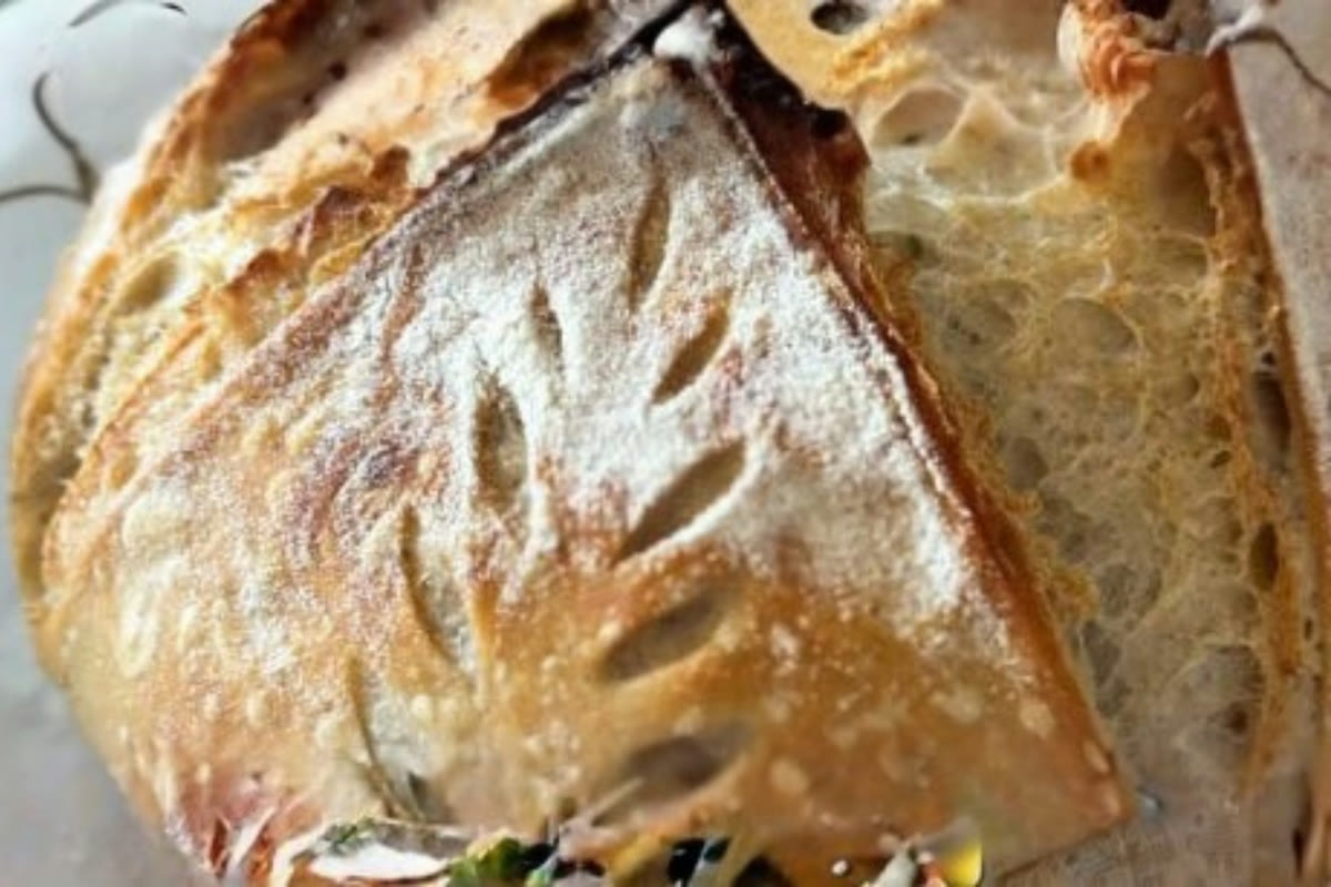 A golden rosemary garlic parmesan loaf beside fresh rosemary and garlic cloves.
